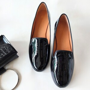 "Business-appropriate women's low-heel moccasins in shiny black leather, a versatile choice for work meetings or weekend brunches."