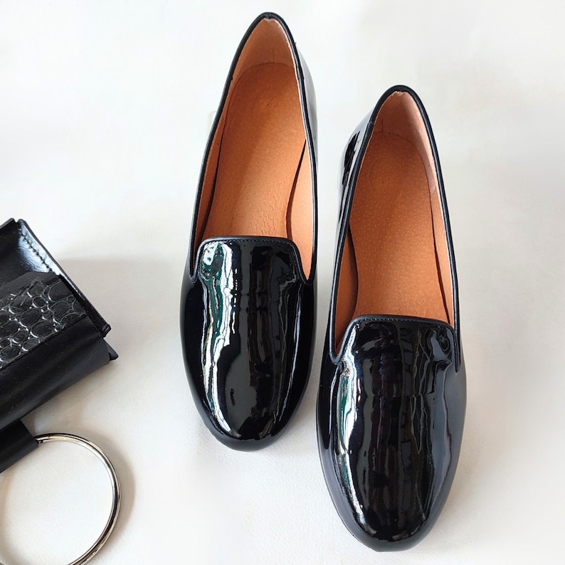"Business-appropriate women's low-heel moccasins in shiny black leather, a versatile choice for work meetings or weekend brunches."