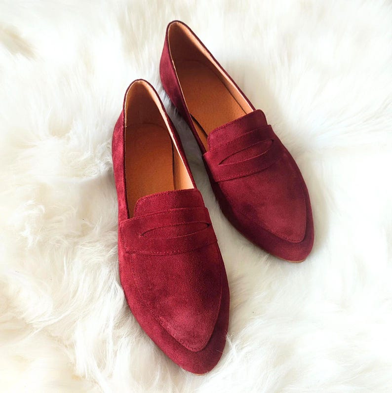 May include: A pair of burgundy suede loafers with a pointed toe and a single strap across the vamp.