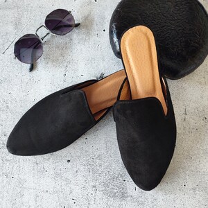 K&ouml;nnte beinhalten: Zwei schwarze Wildlederslipper mit spitzer Zehenpartie und niedrigem Absatz. Die Slipper haben eine braune Ledersohle.