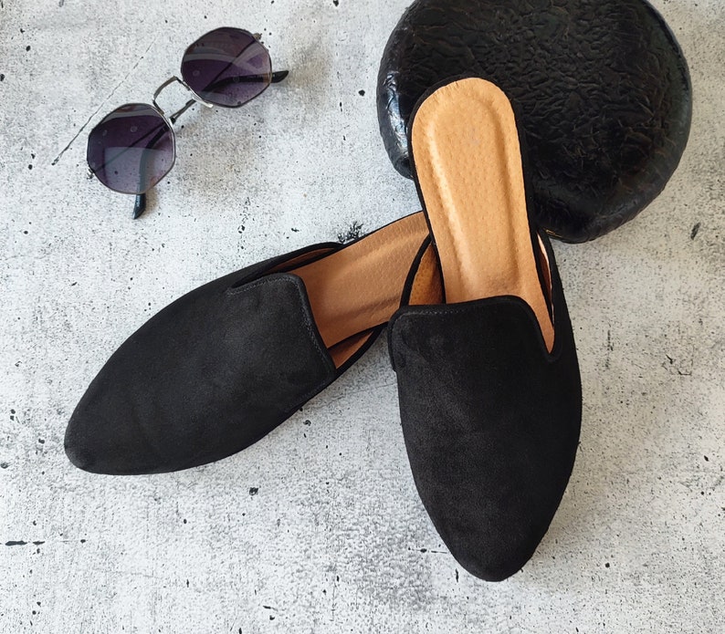 K&ouml;nnte beinhalten: Zwei schwarze Wildlederslipper mit spitzer Zehenpartie und niedrigem Absatz. Die Slipper haben eine braune Ledersohle.
