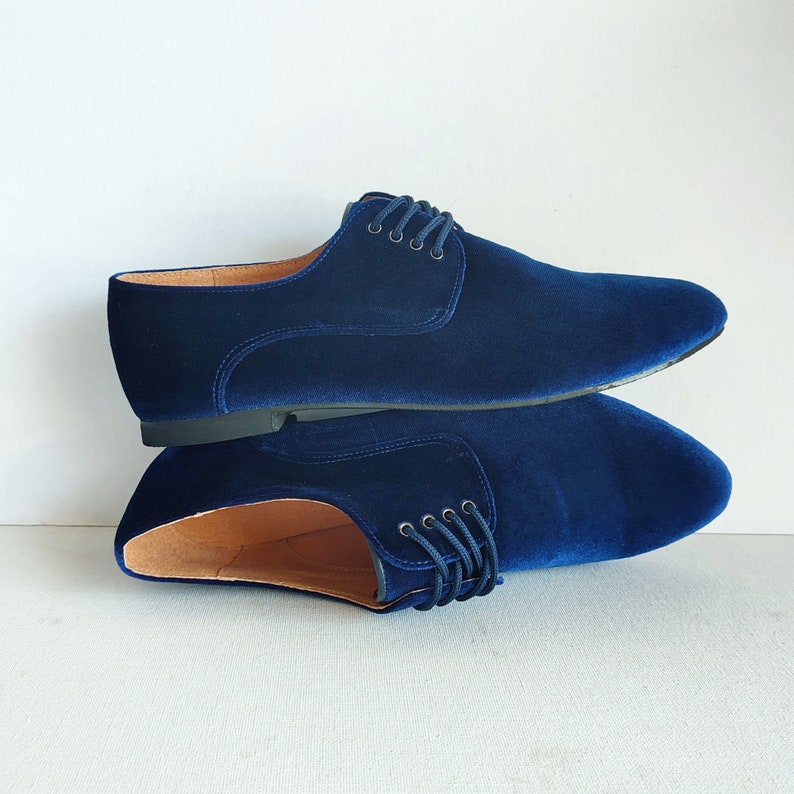 May include: A pair of blue velvet shoes with a lace-up closure. The shoes are stacked on top of each other.