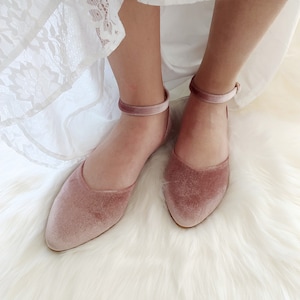 May include: A pair of dusty rose velvet flats with ankle straps. The shoes have a pointed toe and a low heel.