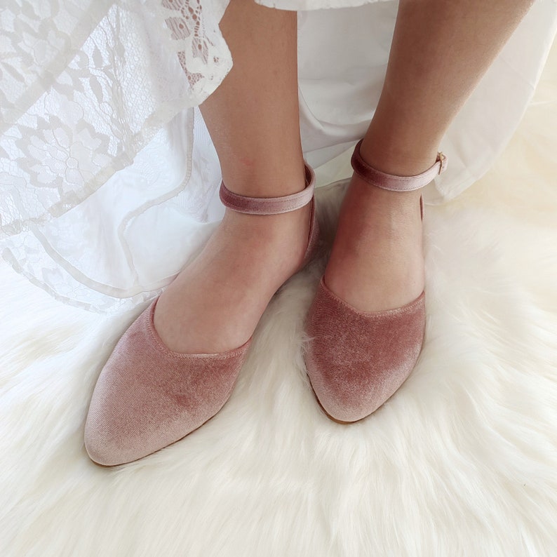 May include: A pair of dusty rose velvet flats with ankle straps. The shoes have a pointed toe and a low heel.