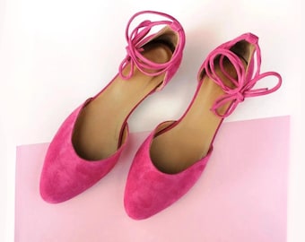 May include: A pair of pink suede ballet flats with ankle ties. The flats have a pointed toe and a low heel.