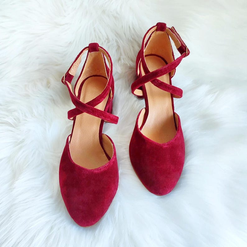 May include: A pair of burgundy velvet heeled shoes with criss-cross straps and ankle buckles.