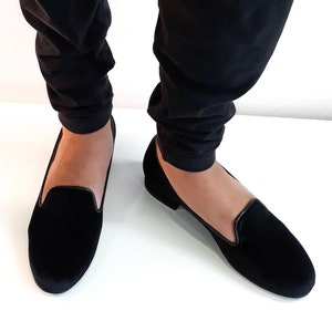 K&ouml;nnte beinhalten: Ein Paar schwarze Samt-Slipper mit dezentem Glanz. Die Slipper haben eine spitze Zehenpartie und einen niedrigen Absatz.