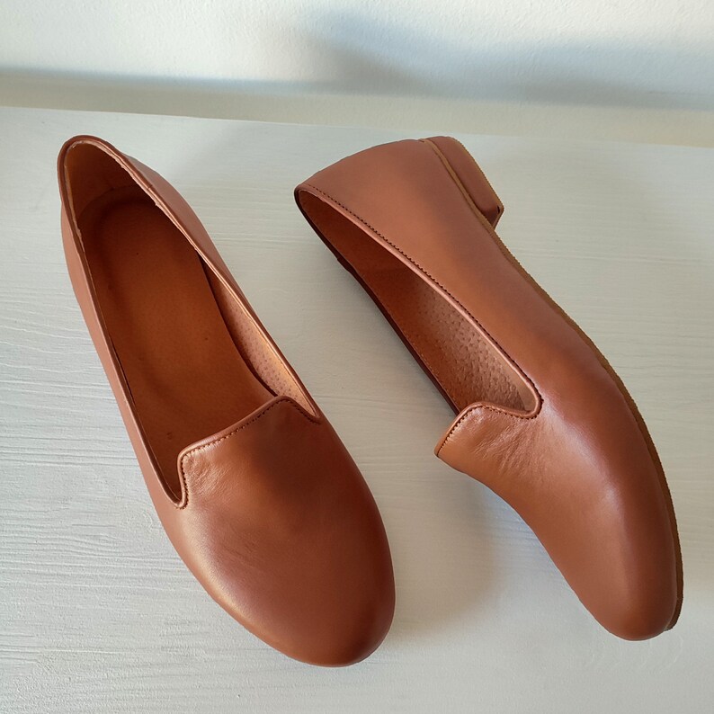 Puede incluir: Un par de mocasines de cuero marr&oacute;n. Los zapatos tienen una punta redondeada y un tac&oacute;n bajo. El cuero tiene una textura suave y un color marr&oacute;n rojizo c&aacute;lido.