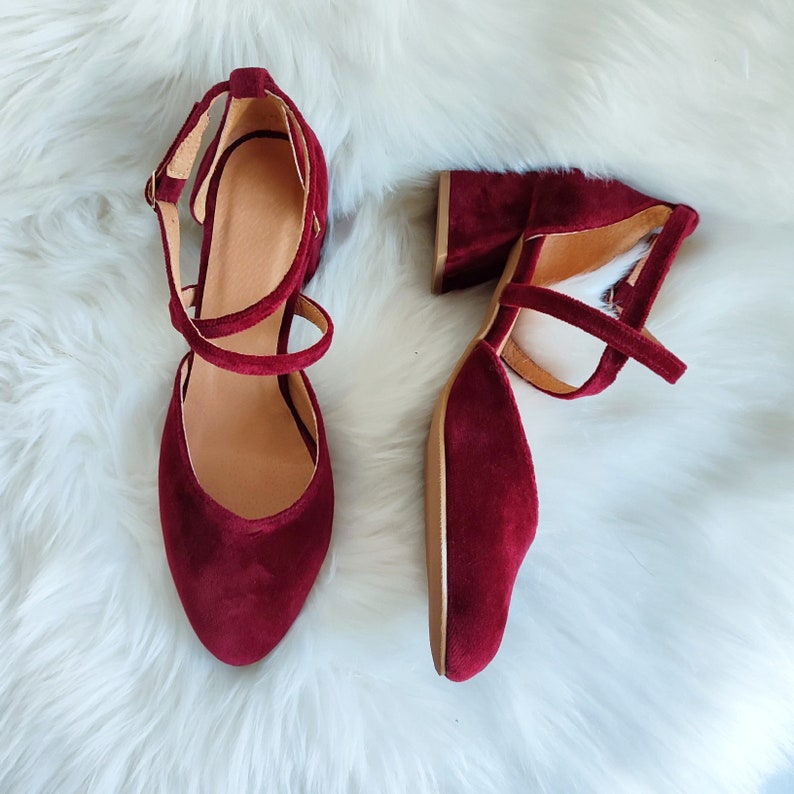 May include: A pair of burgundy velvet heeled shoes with ankle straps. The shoes have a closed toe and a block heel.