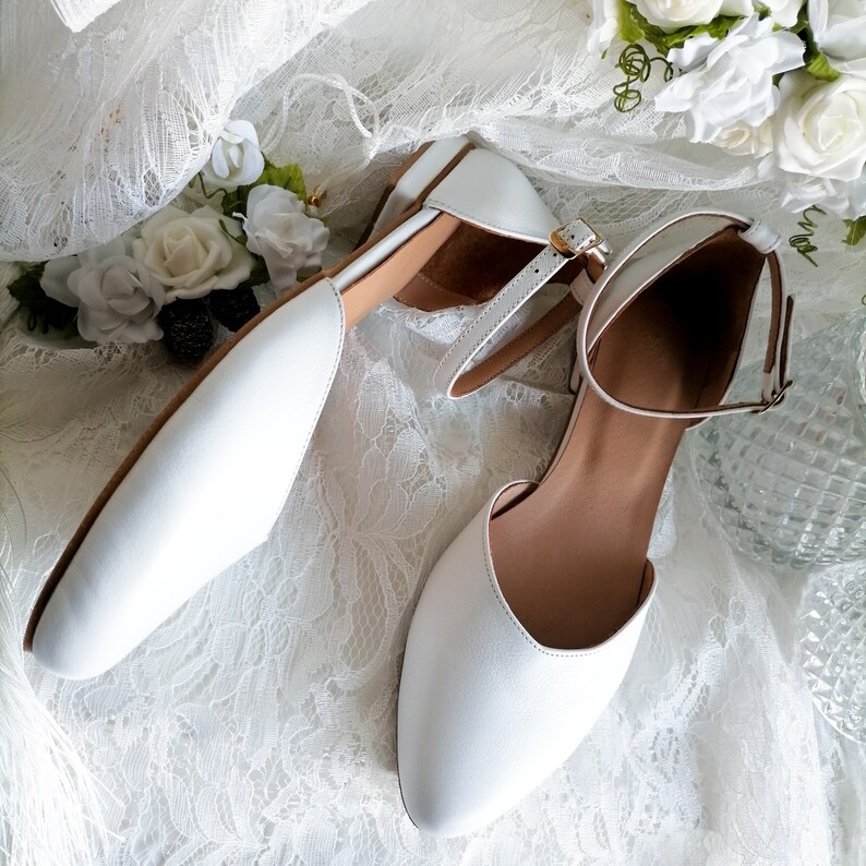 May include: A pair of white leather ankle strap shoes with a pointed toe. The shoes are on a white lace background.