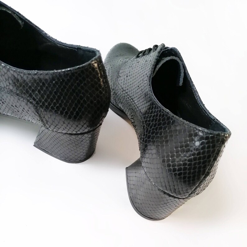 May include: Black leather shoes with a snakeskin pattern. The shoes have a low, block heel and lace-up closure. The heels measure approximately 2 inches.