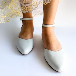 Könnte beinhalten: Ein Paar hellblaue Ballerinas aus Leder mit Knöchelriemen und spitzer Zehenpartie.