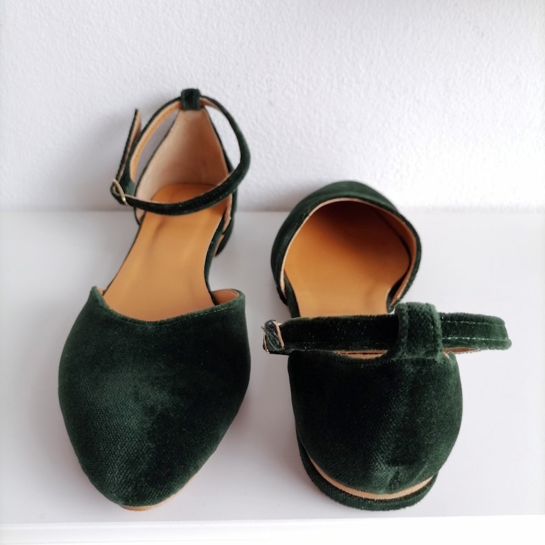 May include: A pair of dark green velvet ankle strap flats. The shoes have a pointed toe and a low heel.