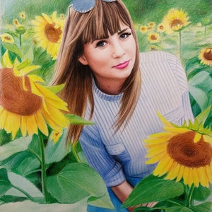Op de afbeelding: Een vrouw met bruin haar en blauwe ogen draagt een zonnebril en een blauw-wit gestreept shirt. Ze staat in een veld met zonnebloemen.