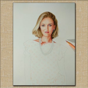 Op de afbeelding: Een vrouw met blond haar draagt een witte blouse met een stippenpatroon. Ze draagt een parelketting en oorbellen. De blouse heeft een gerimpelde kraag en mouwen.