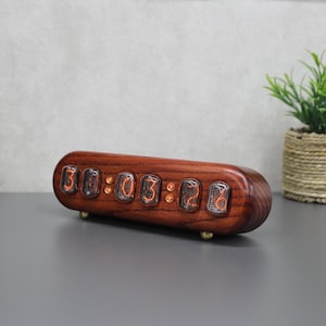 May include: A digital clock with a dark wood finish displays the time 30:03:26. The clock has a rounded rectangular shape and sits on small brass feet. The numbers glow with an orange light.