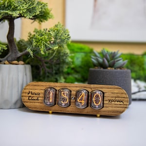 May include: A wooden Nixie clock with a black face and gold accents. The clock displays the time 15:40. The clock is labeled "Nixie Clock" and "xpovos".