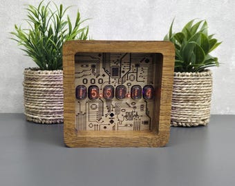 May include: A square wooden nixie tube clock featuring six glowing orange numerical display tubes mounted on a light wood panel with a dark brown printed circuit board pattern and the text "pulsar" in the lower right corner.