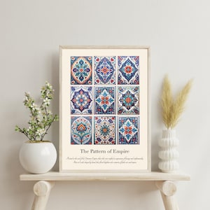 May include: A framed print displaying nine patterned tiles in blue, orange, and white, titled "The Pattern of Empire". The artwork is displayed on a light wooden shelf, alongside a white vase and decorative plants, creating a decorative display.