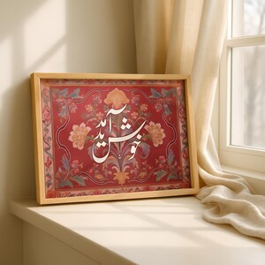 May include: A framed artwork featuring ornate floral patterns in red, peach, and blue. The artwork has a wooden frame and displays elegant white calligraphy. The piece is set against a neutral background, near a window.