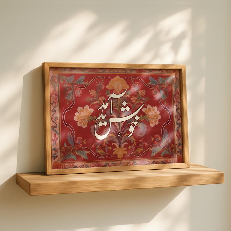 May include: A framed artwork featuring ornate floral patterns in red, yellow, and green. The artwork has a wooden frame and displays white calligraphy. The piece is displayed on a wooden shelf against a neutral wall.