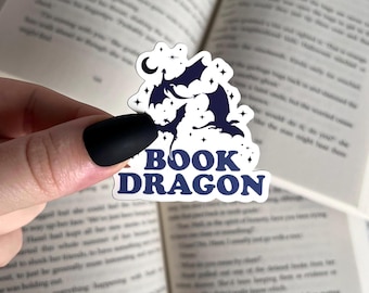May include: A white sticker with a blue silhouette of two dragons flying in front of a crescent moon and stars. The text "BOOK DRAGON" is in blue with a retro font.