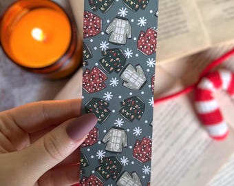 May include: A green bookmark with a repeating pattern of Christmas sweaters with the text "Ho Ho Ho" on them. The sweaters are red, green, and white.