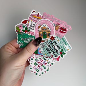 May include: A collection of colorful holiday-themed stickers. Designs include a gingerbread house, a candle, a mug, and text that reads "Holiday TBR," "In My Bookish Christmas Era," and "I'll Be Reading By The Tree."