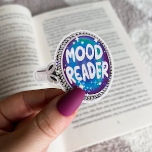 May include: A round sticker with a silver border and a blue, purple, and green galaxy design. The sticker says "MOOD READER" in white text.