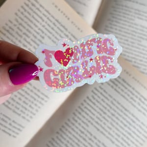 Op de afbeelding: Een witte sticker met een roze en rood glitterontwerp met de tekst "Ik hou van meisjes" met een rood hart in het midden.