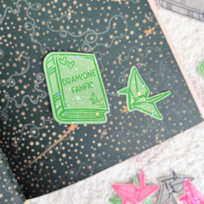 May include: Green book sticker with the text "DRAMIONE FANFIC" and two hearts. A green origami crane sticker is also visible.