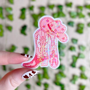 May include: Pink glitter cowboy boots with a pink glitter cowboy hat. The boots and hat have a white outline.