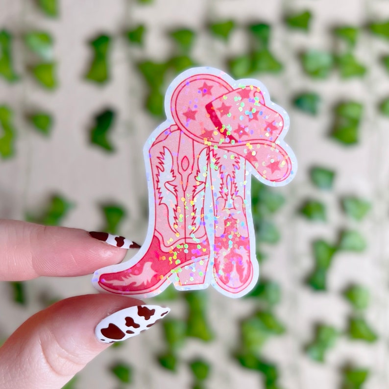May include: Pink glitter cowboy boots with a pink glitter cowboy hat. The boots and hat have a white outline.