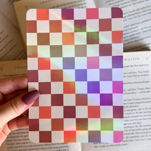 May include: A holographic sticker with a checkered pattern in shades of red, orange, brown, purple, and white.