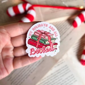 May include: A white sticker with a pink and green illustration of a stack of books tied with a red ribbon. The text on the sticker reads "My Holidays Are All Booked".