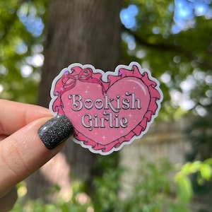 May include: Pink heart-shaped sticker with a white border and the text "Bookish Girlie" in a pink and white font. The sticker has a glittery finish.