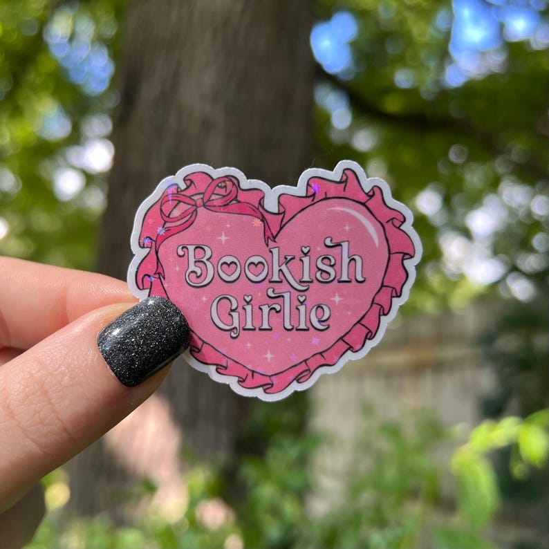 May include: Pink heart-shaped sticker with a white border and the text "Bookish Girlie" in a pink and white font. The sticker has a glittery finish.
