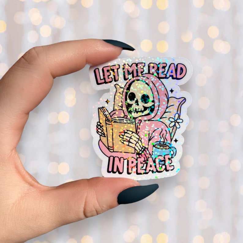 May include: Holographic sticker showing a skeleton in a pink hoodie reading a book, with the text "LET ME READ IN PEACE". The skeleton is holding a book and a cup of coffee. The sticker has a glittery, iridescent finish.