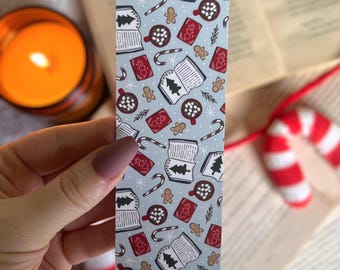 May include: A blue and white bookmark with a repeating pattern of books, mugs of hot chocolate with marshmallows, candy canes, gingerbread men, and Christmas trees.