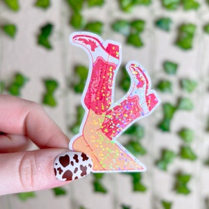 May include: A sticker of a pair of pink cowboy boots with glitter, the boots are upside down and the legs are crossed.