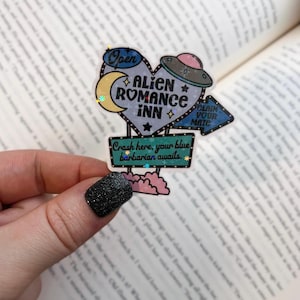 May include: A holographic sticker with a neon sign design that reads "Alien Romance Inn" with a crescent moon, stars, and a UFO. The sign also says "Claim Your Mate" and "Crash here, your blue barbarian awaits."