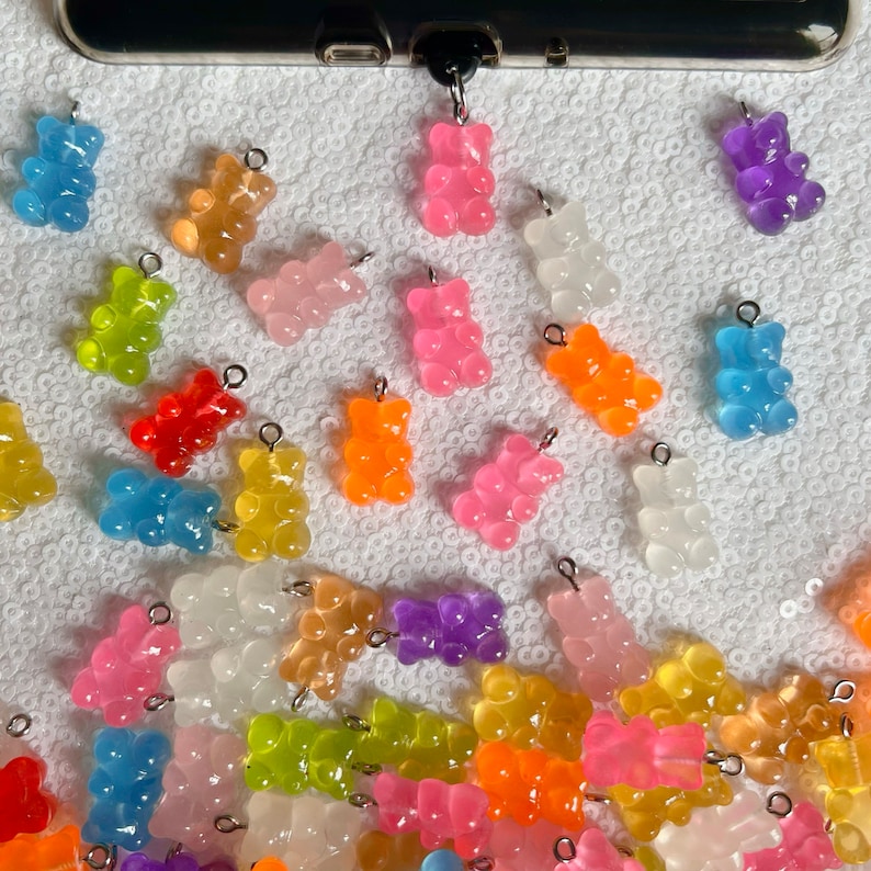 May include: A collection of colorful gummy bear charms, each with a silver loop for attaching to a keychain, necklace, or bracelet. The charms are made of clear plastic and come in a variety of colors, including pink, orange, yellow, green, blue, and purple.