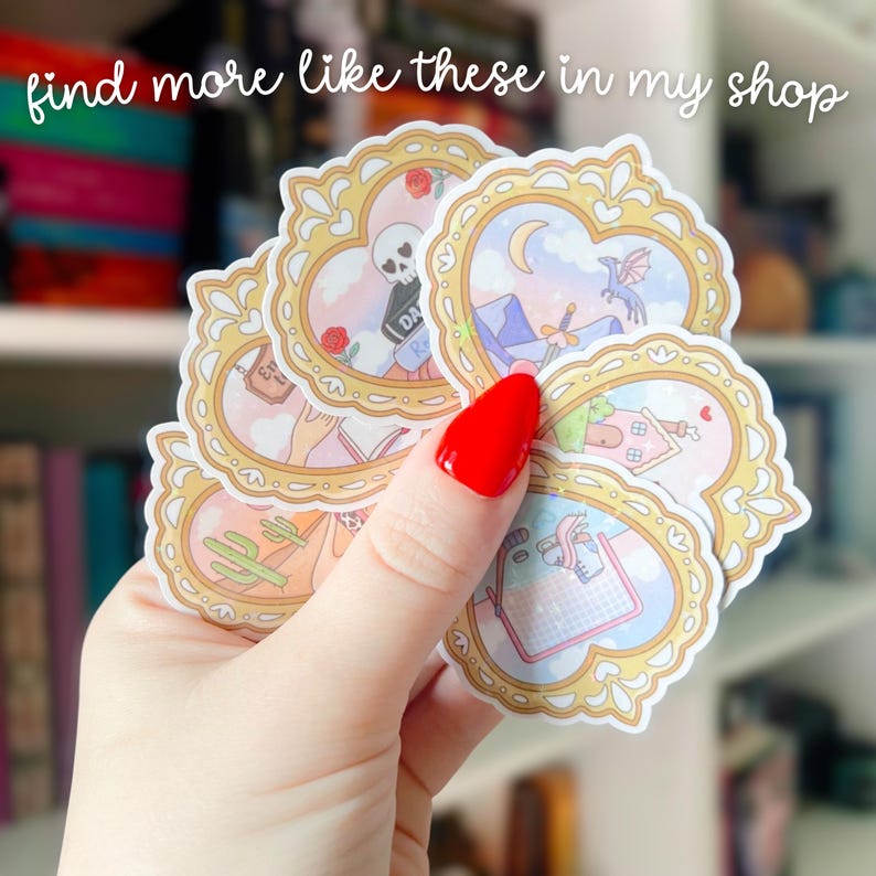 Puede incluir: Una mano sosteniendo una pila de pegatinas decorativas con marcos dorados e ilustraciones en colores pastel. Las pegatinas presentan varios dise&ntilde;os, incluyendo una calavera, un cactus y una casa. El texto "find more like these in my shop" es visible.