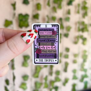 May include: A sticker with a tarot card design featuring the text "The Tropes" and a list of common romance tropes, including "Enemies to Lovers", "Friends to Lovers", "Second Chance", "Forbidden Love", "Only One Bed", "Fake Dating", and "Forced Proximity".