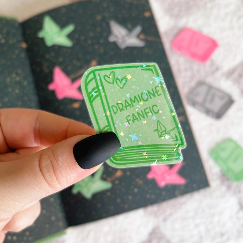 May include: A green book sticker with glitter and the text "DRAMIONE FANFIC" on it.