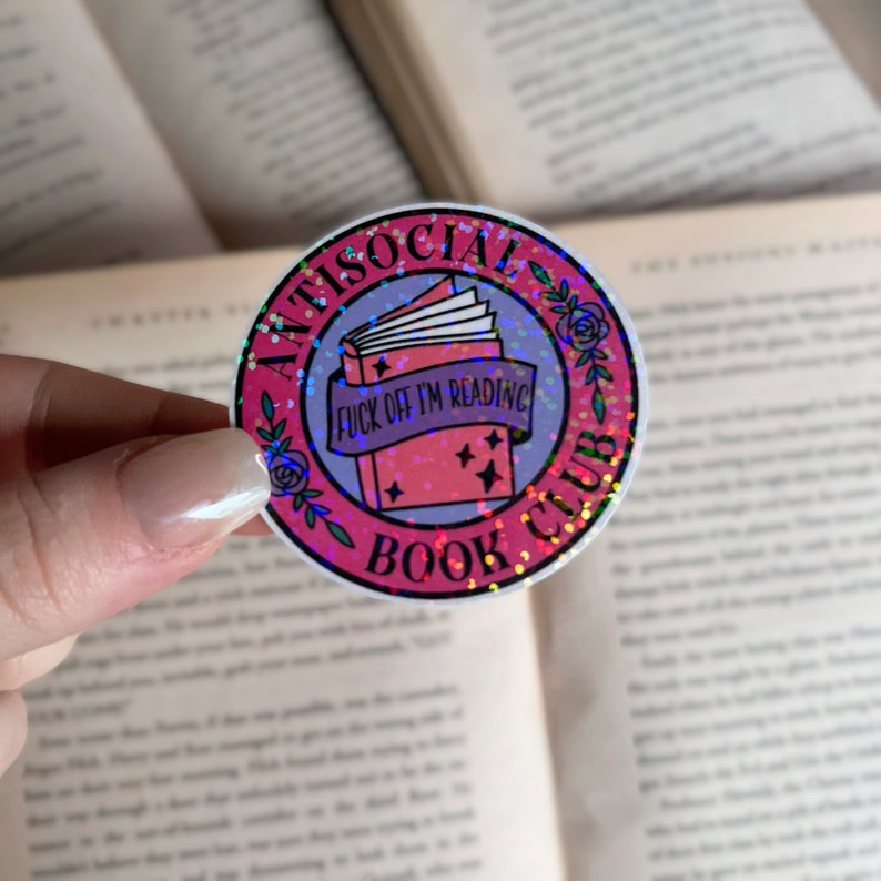 May include: A round sticker with a pink and purple design. The sticker reads "ANTISOCIAL BOOK CLUB" around the edge. The center features a book with a banner that says "FUCK OFF I'M READING".