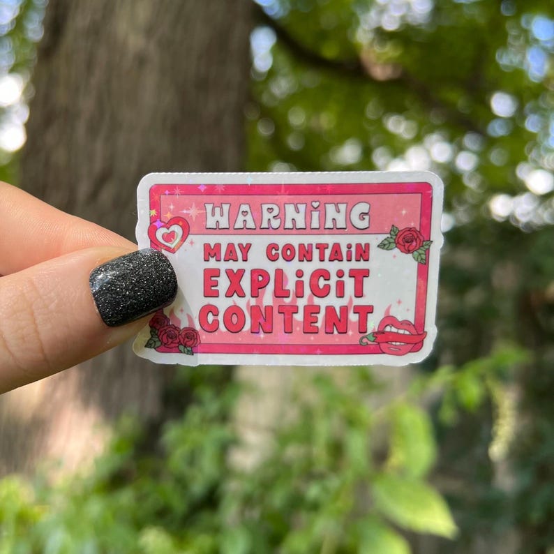 Op de afbeelding: Roze en witte waarschuwingsticker met glitter, een hart, vlammen en een rode lip. De sticker luidt "Waarschuwing Kan expliciete inhoud bevatten".