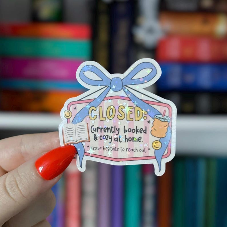 Puede incluir: Una pegatina decorativa con un lazo azul claro y la palabra "CLOSED". La pegatina incluye el texto "Currently booked & cozy at home" e ilustraciones de un libro y una bebida.