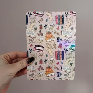May include: A rectangular, patterned case featuring a fall-themed design. The pattern includes illustrations of books, pumpkins, socks, mugs with "hello fall" text, and floral elements in a warm color palette of beige, orange, and brown.