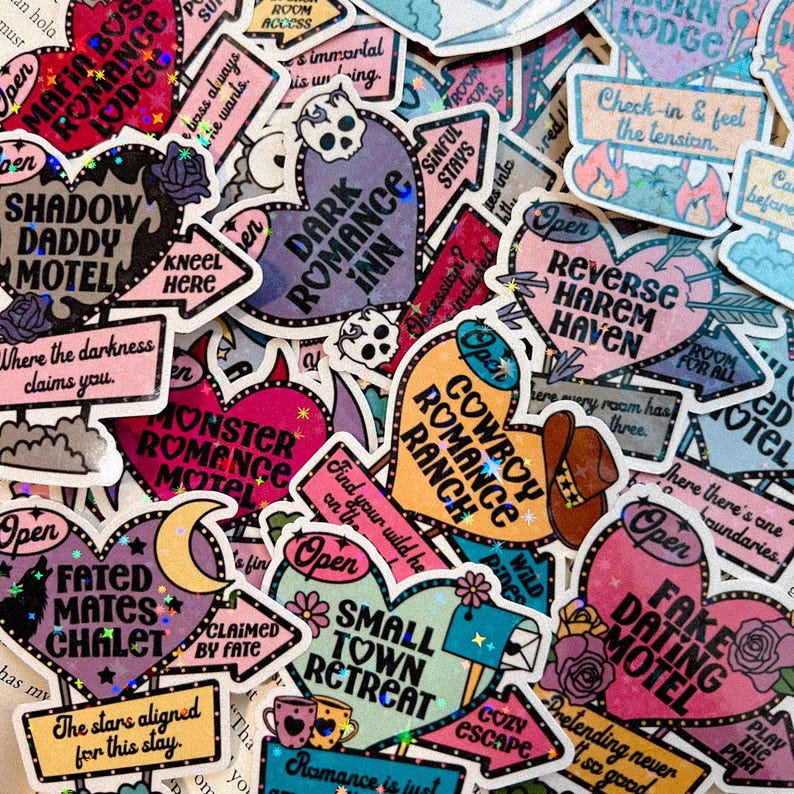 Pu&ograve; includere: Una collezione di adesivi a forma di cuore colorati con vari nomi di motel e resort romantici. Gli adesivi presentano glitter e un'estetica retr&ograve;. Alcuni dei nomi includono "Shadow Daddy Motel", "Dark Romance Inn", "Cowboy Romance Ranch", "Reverse Harem Haven", "Monster Romance Motel", "Small Town Retreat", "Fated Mates Chalet" e "Fake Dating Motel".
